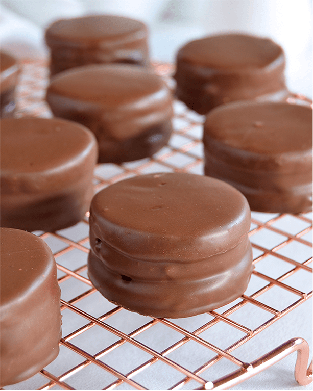 Dark chocolate alfajores on a copper cooling rack